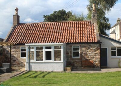 Exterior of a single-storey, stone-built cottage with a red tiled roof.