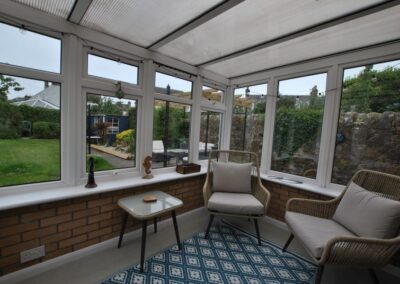 View of garden from sunroom windows. The sun room has a small sofa and chair.