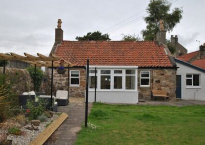 Path leading down the garden towards the house. On the left is a raised bed and patio; on the right is grass.