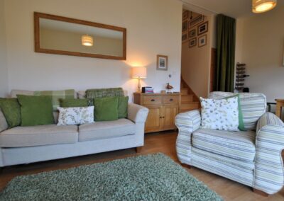 Lounge with wooden floor, rug, sofa and armchar. There are stairs leading upwards in the background.