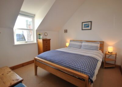 Double bed with blue and white linen beneath a sloping ceiling with a dormer window to the left.