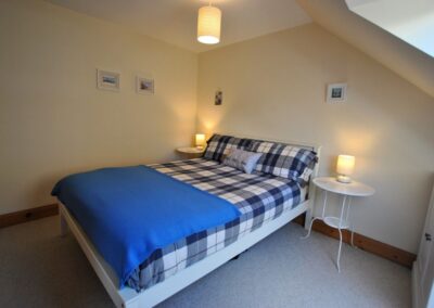 White double bedframe with checkered blue and white linen, with white, round bedside tables and lamps either side.