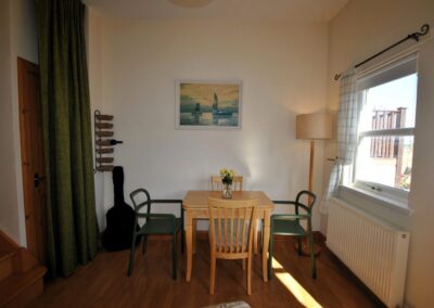 Square wooden table with four chairs. The dining room has a large window and a standard lamp.