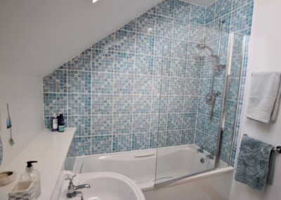 Shower over bath, surrounded by tiles and transparent shower screen.