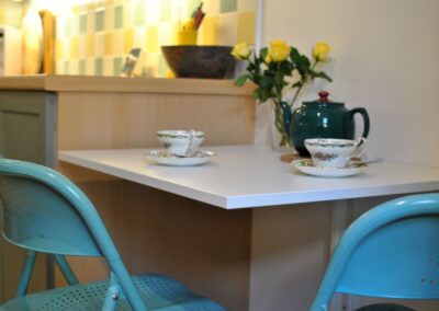 Close up of two tea cups and teapot on a small table with light blue, metal folding chairs.