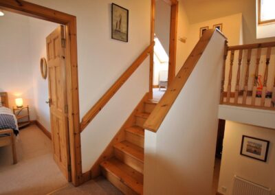 View from landing between floors with open door to bedroom on the left, stairs up to another room and stairs down.