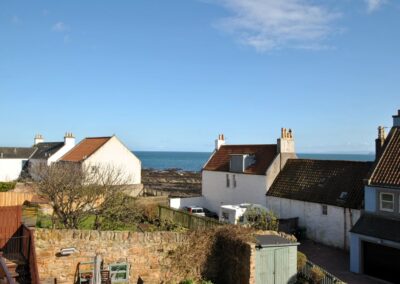 View across gardens and rooftops to the sea between two houses opposite.