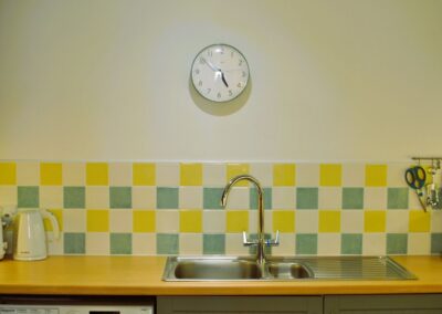 Wall clock above itchen sink. Splashback tiles are white, yellow and green.