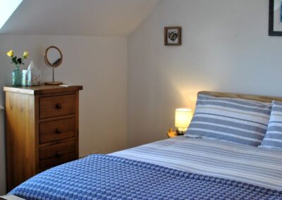 Bed dressed in blue and white linen with a thin drawer unit to the right of a window.