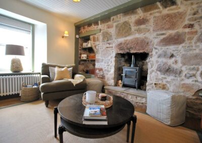 Bare stone wall around fireplace, round coffee table and armchair.