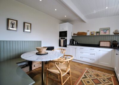 Corner seating around a circular table in a green and white wooden kitchen.