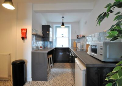 The galley kitchen has dark counters and light tiles. There is a window at the far end.