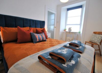 Double bed with blue headboard, orange pillows and duvet cover.