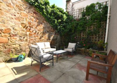 Garden chairs and table on patio surrounded by tall stone walls and foliage.