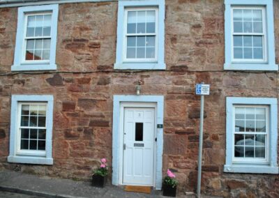 Stone building with five windows and white door.