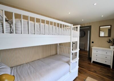 View of white, wooden bunks on left and three drawer chest of drawers to the right of an open door.