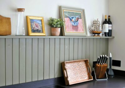 Close-up of kitchen counter with tray, knife rack and a shelf with artwork and wine bottles.