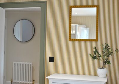 Round mirror in the hallway; square mirror in the bedroom against a striped wallpaper.