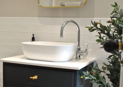 White bowl-like sink with chrome mixer tap beside foliage.