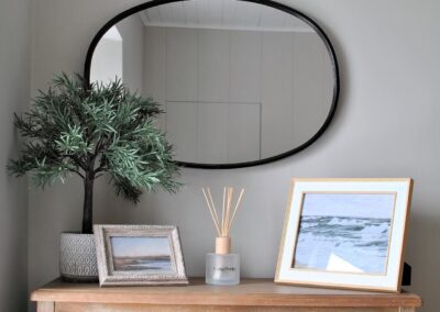 Oval wall mirror above potted plant and framed artwork.