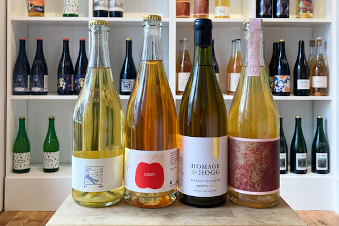 Four bottles of cider in front of shelves of bottles.