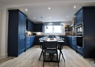 Dark blue kitchen units wrap around a long dining table.