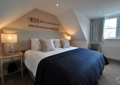 Large bed beneath a sloping ceiling with oars on the wall above the bed. To the right is a window.