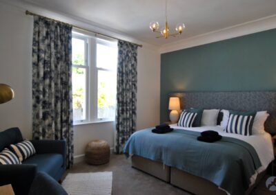 Single beds placed together. There is a large window with long curtains and to the left of it an armchair.