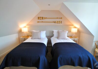 Single beds beneath a sloping ceiling. Two oars are fixed to the wall above the beds. There is a window to the right.