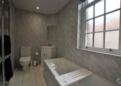 Tiled bathroom with white suite. The bath sits beneath a window, parallel to the wall.