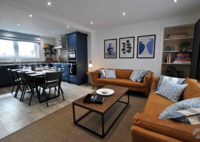 Kitchen and dining area to the left, orange-brown sofas on the right around a coffee table with blue and white artwork on the wall.