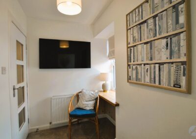 TV on wall to the right of the door, next to a desk and chair in front of a window.