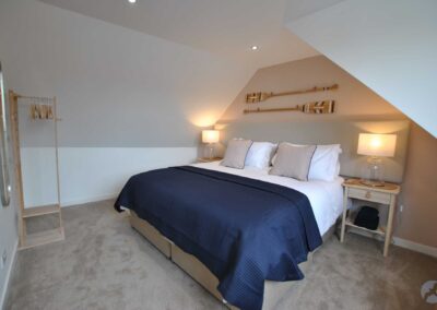 Bedroom decorated with neutral colours, with a deep navy bedspread and oars on the wall.