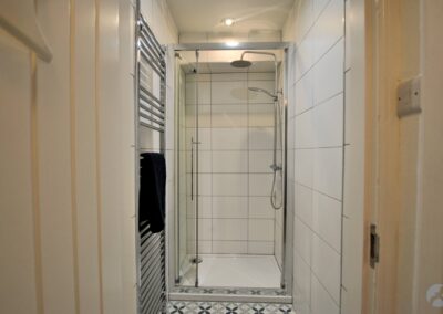 Shower room with white tiled walls and a tall chrome heated towel rail.