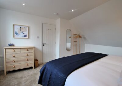 View across bed towards door. There is a chest of drawers on the left and a long mirror and clothes unit on the right.